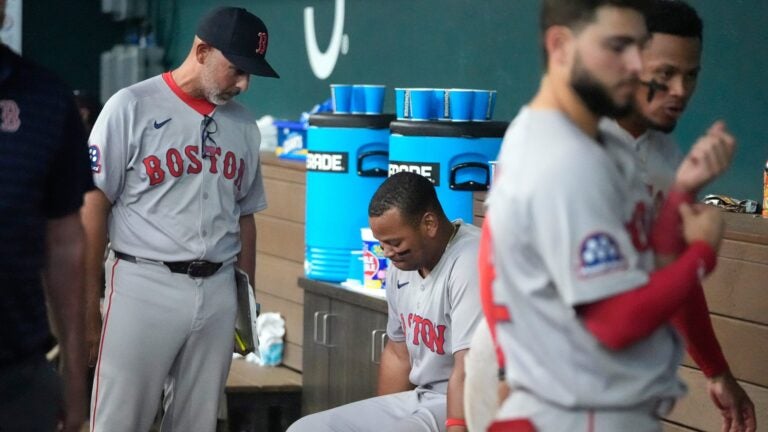 Alex Cora stands while talking to Rafael Devers, who is seated on the dugout bench.
