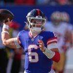 Giants quarterback Jaxson Dart readies to throw a pass with a football in hand and his arm bent back.